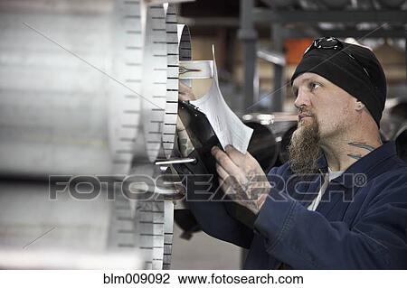 Stock Image - Caucasian man examining metal pipe in factory. Fotosearch