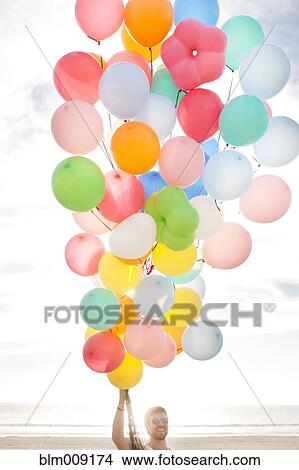 Picture - Caucasian man holding balloons on beach. Fotosearch