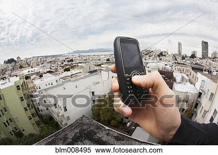 Caucasian man holding cell phone with cityscape in background View Large Photo Image Stock Photography - Caucasian man holding cell phone with cityscape in background. Fotosearch