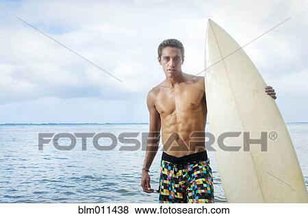 Stock Photo - Caucasian man holding surfboard near ocean. Fotosearch