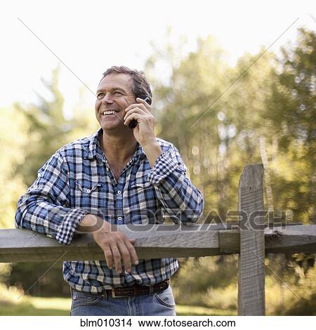 Caucasian man leaning on fence talking on cell phone View Large Photo Image Picture - Caucasian man leaning on fence talking on cell phone. Fotosearch