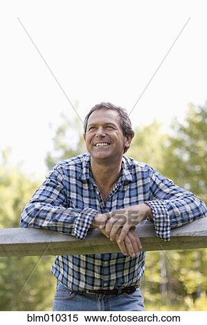 Stock Photography - Caucasian man leaning on wooden fence. Fotosearch