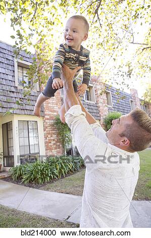 Stock Image - Caucasian man playing with son outdoors. Fotosearch
