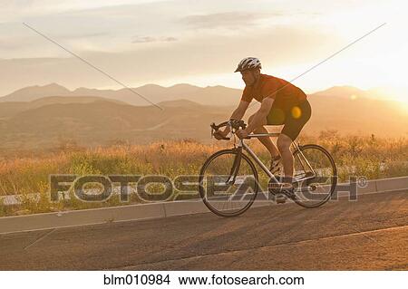 Picture - Caucasian man riding bicycle on remote road. Fotosearch