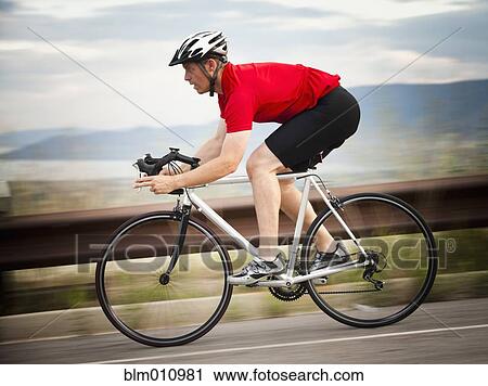 Stock Image - Caucasian man riding bicycle on remote road. Fotosearch