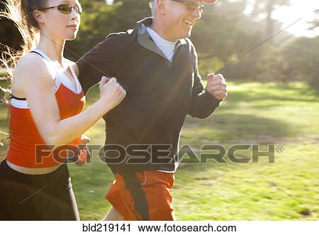 Stock Image - Caucasian man running with trainer in field. Fotosearch