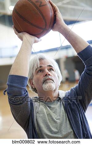 Stock Image - Caucasian man shooting basketball in gym. Fotosearch