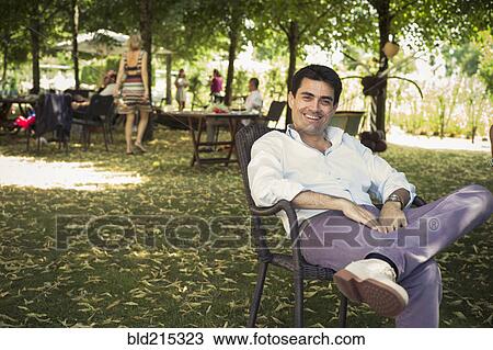 Stock Image - Caucasian man sitting in chair in backyard. Fotosearch