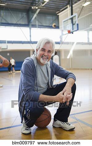 Stock Photo - Caucasian man sitting on basketball in gym. Fotosearch