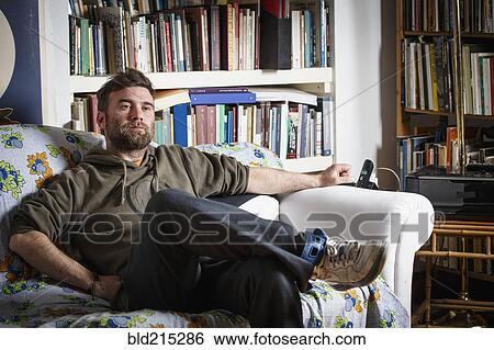 Caucasian man sitting on sofa in living room View Large Photo Image Stock Photograph - Caucasian man sitting on sofa in living room. Fotosearch