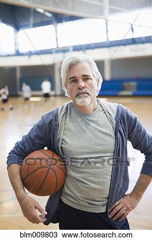 Stock Image - Caucasian man standing in gym with basketball. Fotosearch