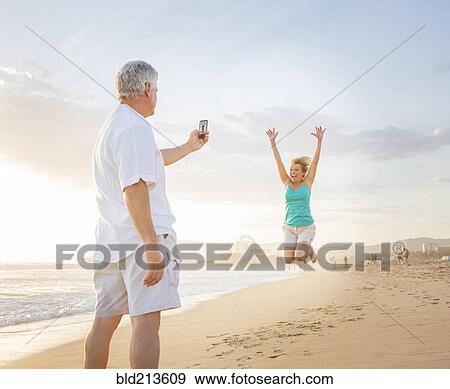 Caucasian man taking cell phone photograph of wife on beach View Large Photo Image Stock Photo - Caucasian man taking cell phone photograph of wife on beach. Fotosearch
