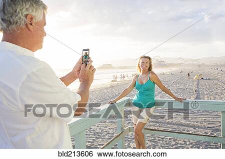 Caucasian man taking photograph of wife on boardwalk at beach View Large Photo Image Stock Photograph - Caucasian man taking photograph of wife on boardwalk at beach. Fotosearch