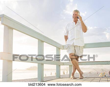 Caucasian man talking on cell phone on boardwalk at beach View Large Photo Image Picture - Caucasian man talking on cell phone on boardwalk at beach. Fotosearch