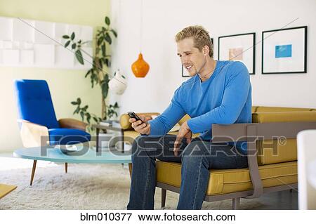 Stock Photo - Caucasian man text messaging on cell phone in living room. Fotosearch