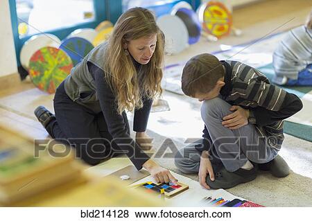 Stock Photo - Caucasian Montessori teacher helping student in classroom. Fotosearch