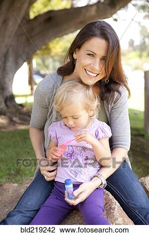 Stock Image - Caucasian mother and daughter blowing bubbles outdoors. Fotosearch