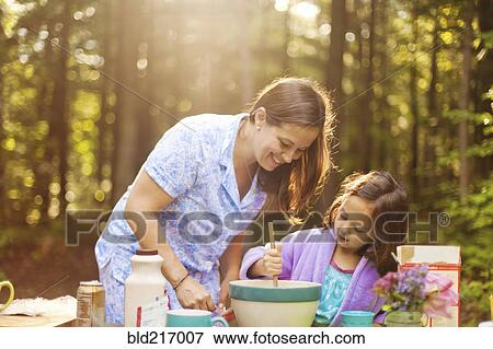 Stock Photo - Caucasian mother and daughter cooking in forest. Fotosearch