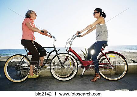 Stock Image - Caucasian mother and daughter riding bicycles near beach. Fotosearch