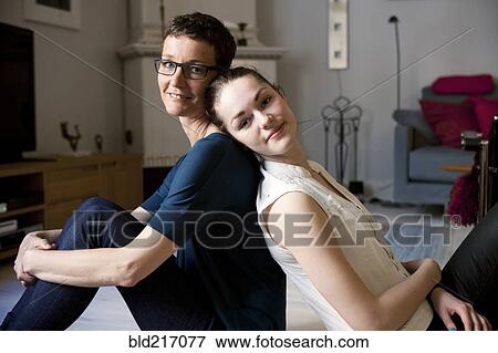 Stock Photo - Caucasian mother and daughter sitting back to back. Fotosearch