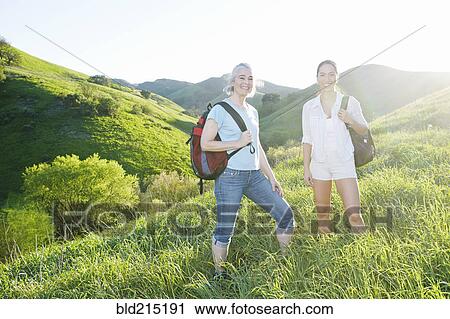 Stock Image - Caucasian mother and daughter smiling on grassy hillside. Fotosearch