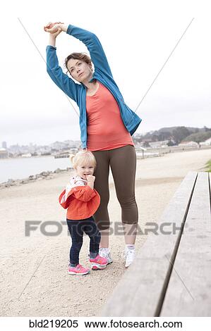 Stock Photography - Caucasian mother and daughter stretching on beach. Fotosearch