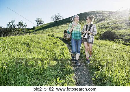 Stock Image - Caucasian mother and daughter walking on grassy hillside. Fotosearch