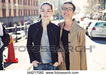 Stock Image - Caucasian mother and daughter walking on city sidewalk. Fotosearch