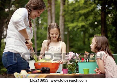 Stock Image - Caucasian mother and daughters cooking outdoors. Fotosearch