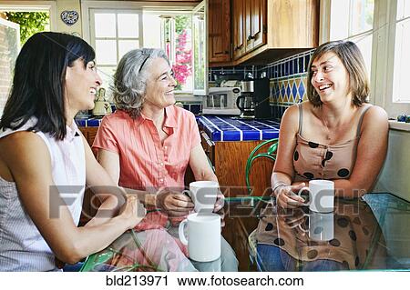 Stock Image - Caucasian mother and daughters drinking coffee in kitchen. Fotosearch