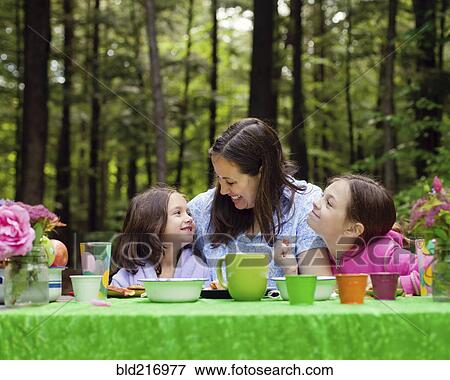 Stock Photo - Caucasian mother and daughters sitting at table outdoors. Fotosearch