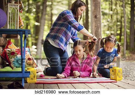 Stock Image - Caucasian mother brushing hair of daughter on porch. Fotosearch