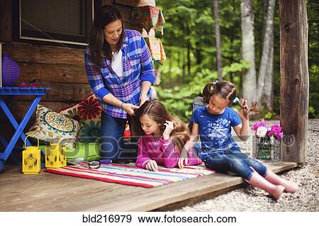 Stock Photo - Caucasian mother brushing hair of daughter on porch. Fotosearch