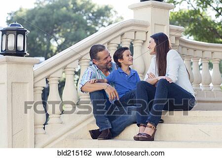 Stock Image - Caucasian mother, father and son relaxing on front stoop. Fotosearch