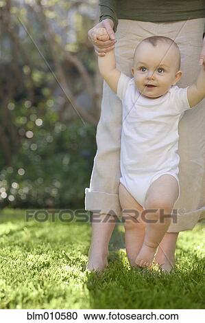Caucasian mother helping baby to walk in grass View Large Photo Image Stock Image - Caucasian mother helping baby to walk in grass. Fotosearch