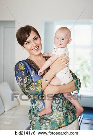 Caucasian mother holding baby in living room View Large Photo Image Stock Photograph - Caucasian mother holding baby in living room. Fotosearch