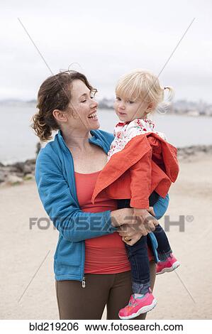 Stock Photograph - Caucasian mother holding daughter on beach. Fotosearch
