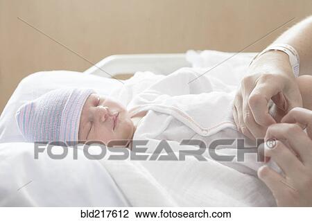 Stock Image - Caucasian mother holding newborn daughter in hospital bed. Fotosearch
