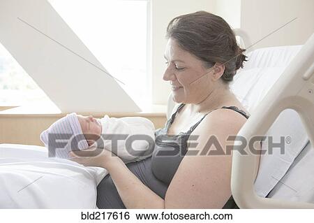 Stock Photograph - Caucasian mother holding newborn daughter in hospital bed. Fotosearch