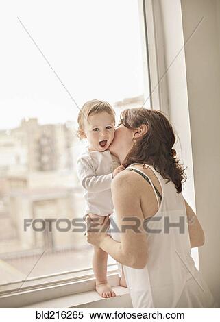 Stock Photography - Caucasian mother kissing baby in window. Fotosearch