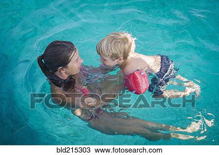 Stock Image - Caucasian mother teaching son to swim in pool. Fotosearch