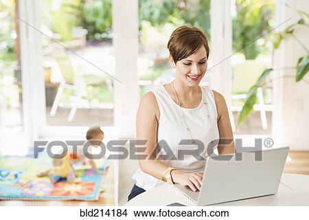 Picture - Caucasian mother using laptop at counter. Fotosearch
