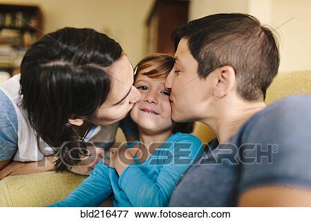 Stock Photo - Caucasian mothers kissing daughter in living room. Fotosearch
