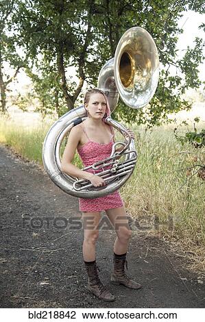 Stock Image - Caucasian musician carrying tuba on dirt path. Fotosearch