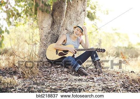 Stock Photo - Caucasian musician holding guitar under tree. Fotosearch