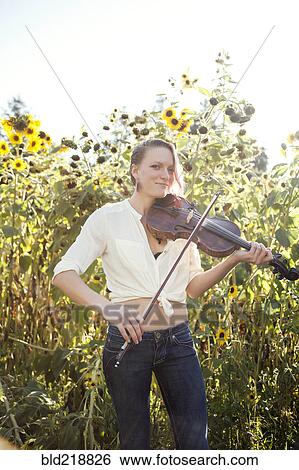 Stock Photograph - Caucasian musician playing violin in sunflower garden. Fotosearch