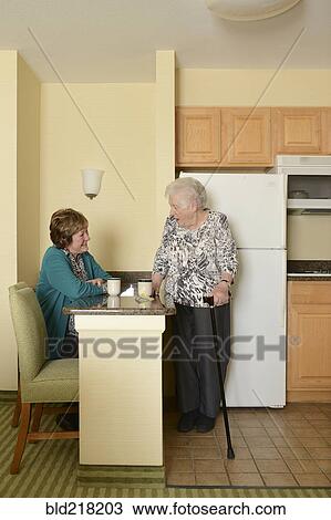 Stock Image - Caucasian older women relaxing in kitchen. Fotosearch