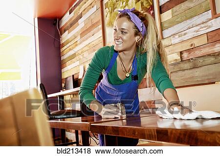 Stock Photo - Caucasian server wiping down tables in cafe. Fotosearch