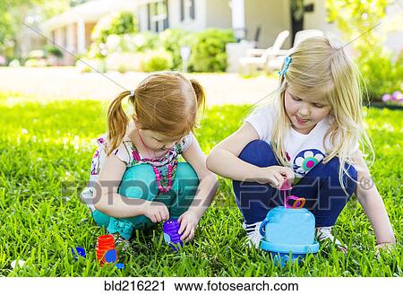 Stock Image - Caucasian sisters blowing bubbles in backyard. Fotosearch