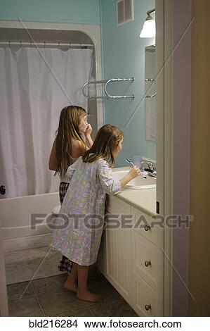 Picture - Caucasian sisters brushing teeth in bathroom. Fotosearch